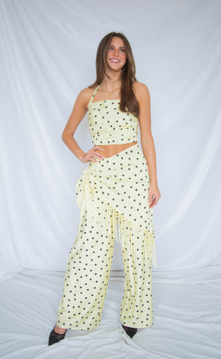 Woman wearing a cream polka dot two piece outfit with fringe details on a white background