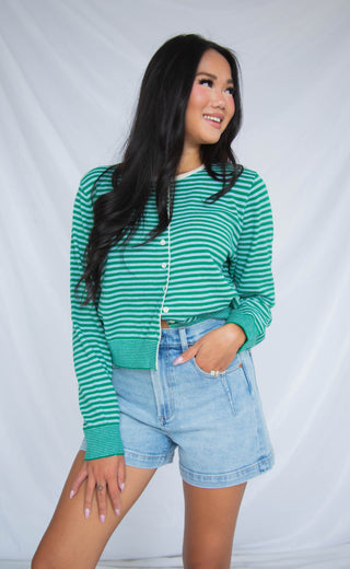 Woman wearing a green and white striped sweater and denim shorts against a plain background