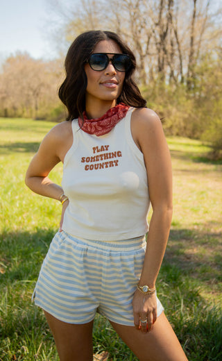 Woman wearing a sleeveless tank top with "play something country" text and shorts outdoors