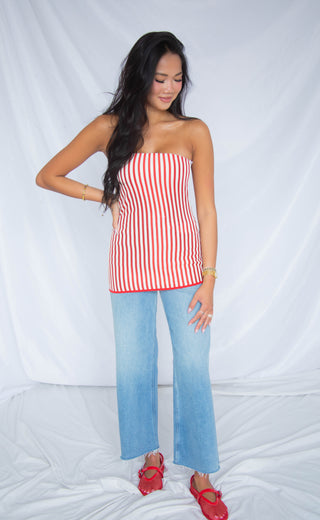 Woman wearing a red and white striped tube top and blue jeans against a white background