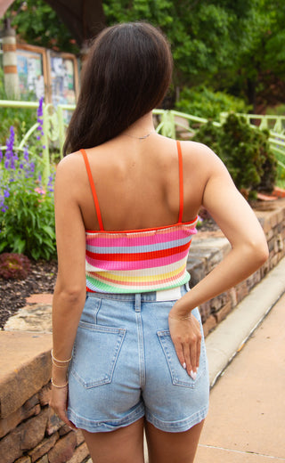 Person wearing a colorful striped tank top and denim shorts in an outdoor setting.
