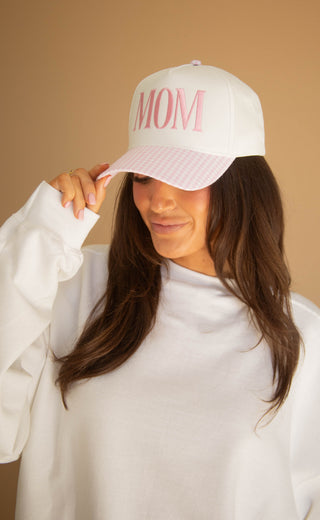 Woman wearing a white and pink gingham trucker hat with 'MOM' text on a beige background