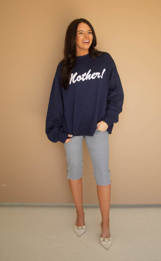 Woman wearing a navy mockneck sweatshirt with 'Mother!' text, standing against a beige wall.