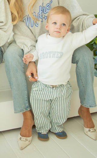 Child wearing a 'BROTHER' sweatshirt sitting on a person's lap.