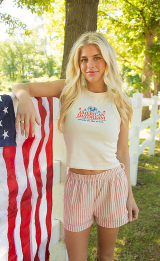 Woman wearing a 'American Daydream' halter tank top standing next to an American flag outdoors.