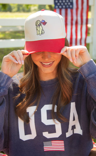 Woman wearing a cap with a dog design and American flag, standing in front of an American flag.