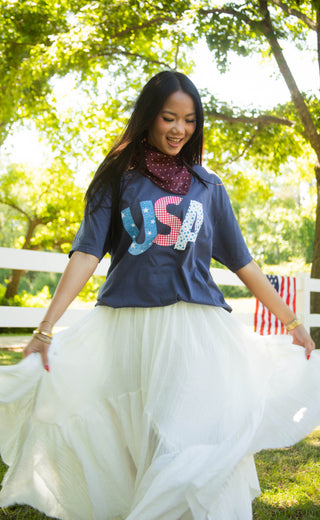 Woman wearing a 'USA' shirt and white skirt in a park setting