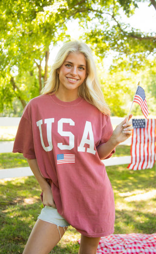 Woman wearing a 'USA' t-shirt outdoors with American flags in the background