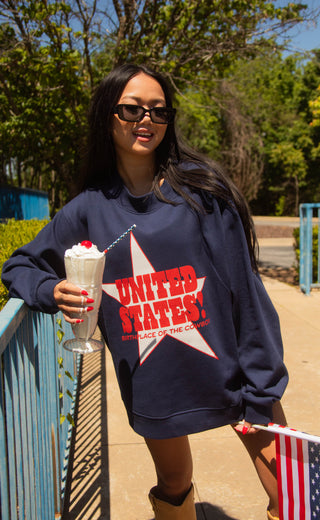 Person wearing a navy sweatshirt with 'UNITED STATES' text, holding a milkshake and an American flag.