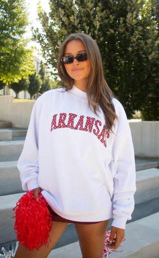 A woman wearing a white long-sleeve sweatshirt with 'ARKANSAS' in red star-style lettering.