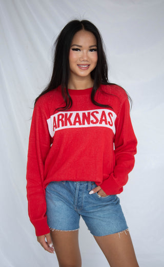 Person wearing a red 'ARKANSAS' sweater with denim shorts on a white background