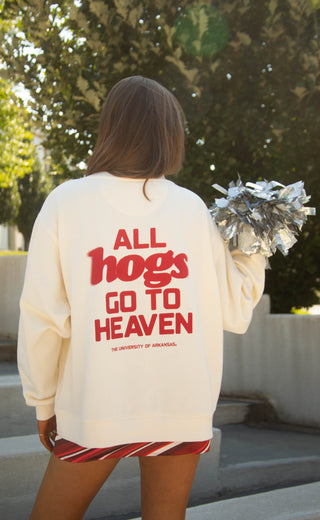A woman viewed from behind wearing an off-white sweatshirt with red text that reads 'ALL hogs GO TO HEAVEN' and 'THE UNIVERSITY OF ARKANSAS' underneath. 