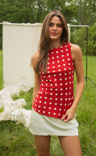 Woman wearing a red polka dot top standing outdoors in a grassy area.
