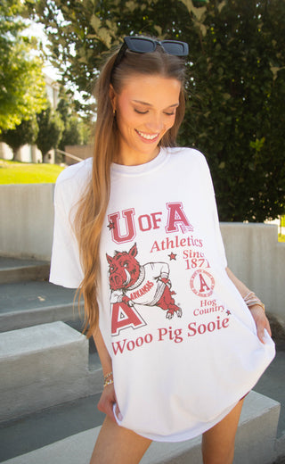 A woman wearing an oversized white graphic T-shirt with red text reading 'U of A Athletics Since 1871' and 'Wooo Pig Sooie,' plus a pig mascot illustration.