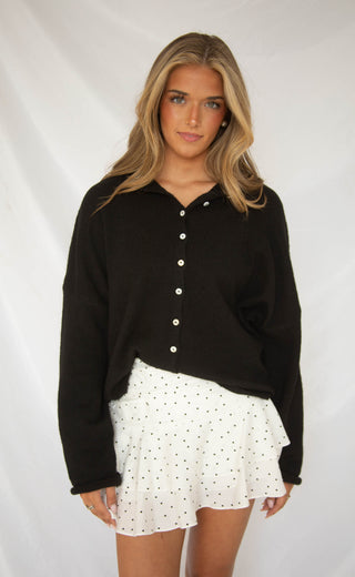 Woman wearing a black button-up shirt and white polka dot skirt.