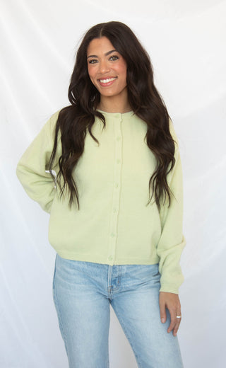 Woman wearing a light green cardigan and blue jeans against a white background