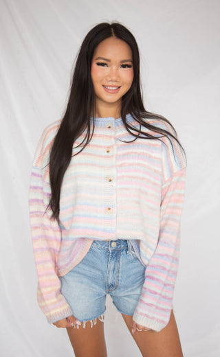 Woman wearing a pastel striped cardigan and denim shorts on a white background