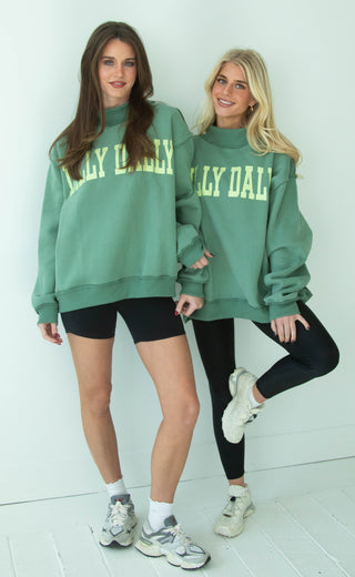 Two women wearing green mock neck sweatshirts with 'DILLY DALLY' text, standing side by side on a white background.