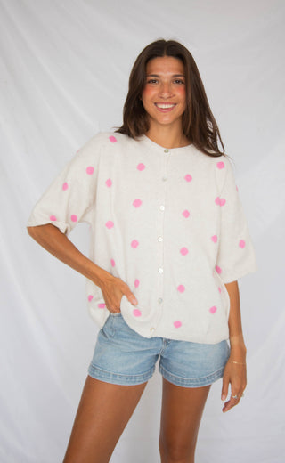 Woman wearing a white blouse with pink polka dots and denim shorts on a plain background