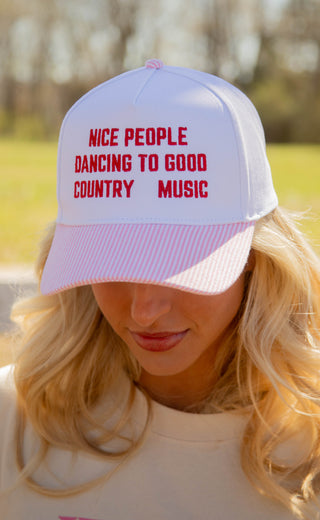 Person wearing a trucker hat with text 'Nice people dancing to good country music' outdoors.
