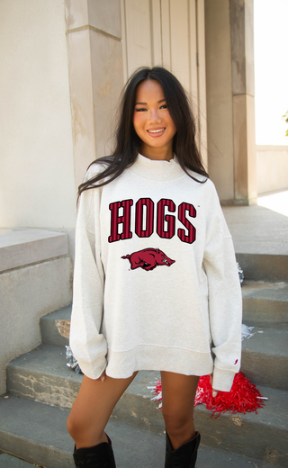 A woman wearing an oversized off-white sweatshirt with 'HOGS' and a red razorback logo printed on the front, standing on outdoor stone steps.