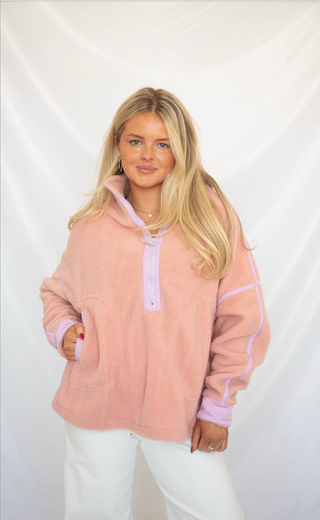 Woman wearing a pink sherpa pullover jacket with white pants on a plain background