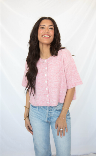 Woman wearing a pink short sleeve cardigan shirt and light blue jeans against a white background