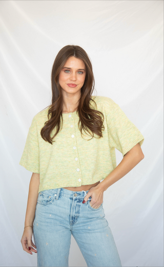 Woman wearing a light green short sleeve cardigan shirt and blue jeans against a white background