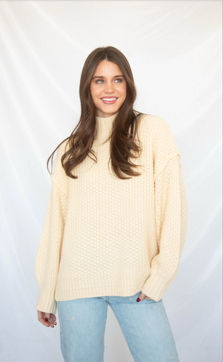 Woman wearing a cream sweater and light blue jeans against a white background