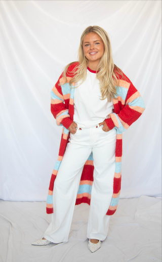 Woman wearing a colorful striped cardigan over a white outfit on a plain background