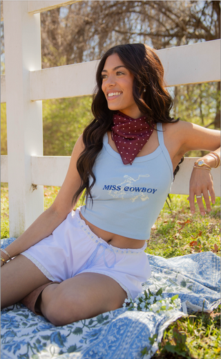 Woman sitting on a blanket outdoors wearing a 'Miss Cowboy' tank top.