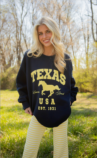 Woman wearing a navy sweatshirt with yellow 'Texas USA' text and horse graphic outdoors.