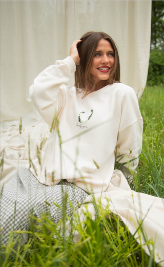 Woman wearing a white sweatshirt with a design, sitting in a grassy area.