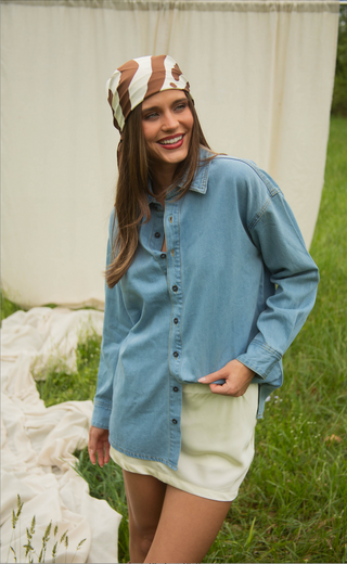 Woman wearing a blue denim shirt over a white dress with a headband, standing outdoors.