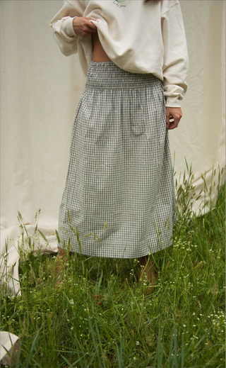 Women wearing a checkered skirt standing in grass with a neutral background