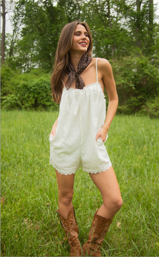 Woman in a white romper with brown boots standing in a grassy field.