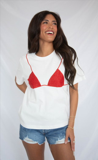 Woman wearing a white t-shirt with a red bikini graphic and denim shorts on a plain background