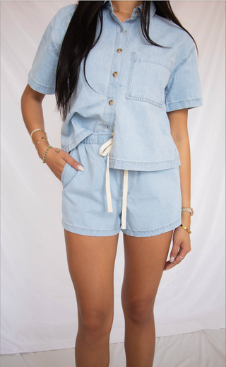 Person wearing a light blue denim outfit with shorts and a jacket on a white background