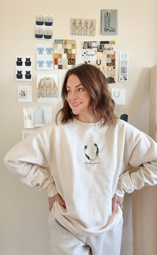 Person wearing a white sweatshirt with a logo and text, standing in a room with wall art.
